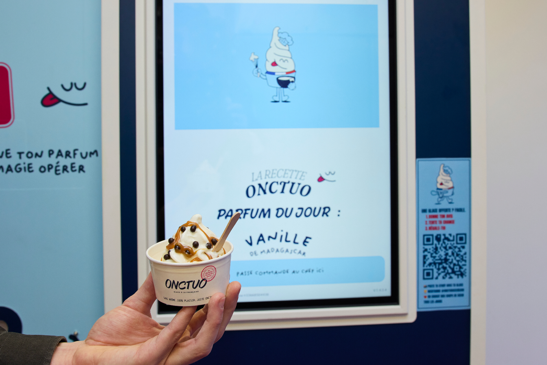 Pot de glace à l'italienne ONCTUO à la vanille de Madagascar, caramel et perles de chocolat, devant une machine ONCTUO